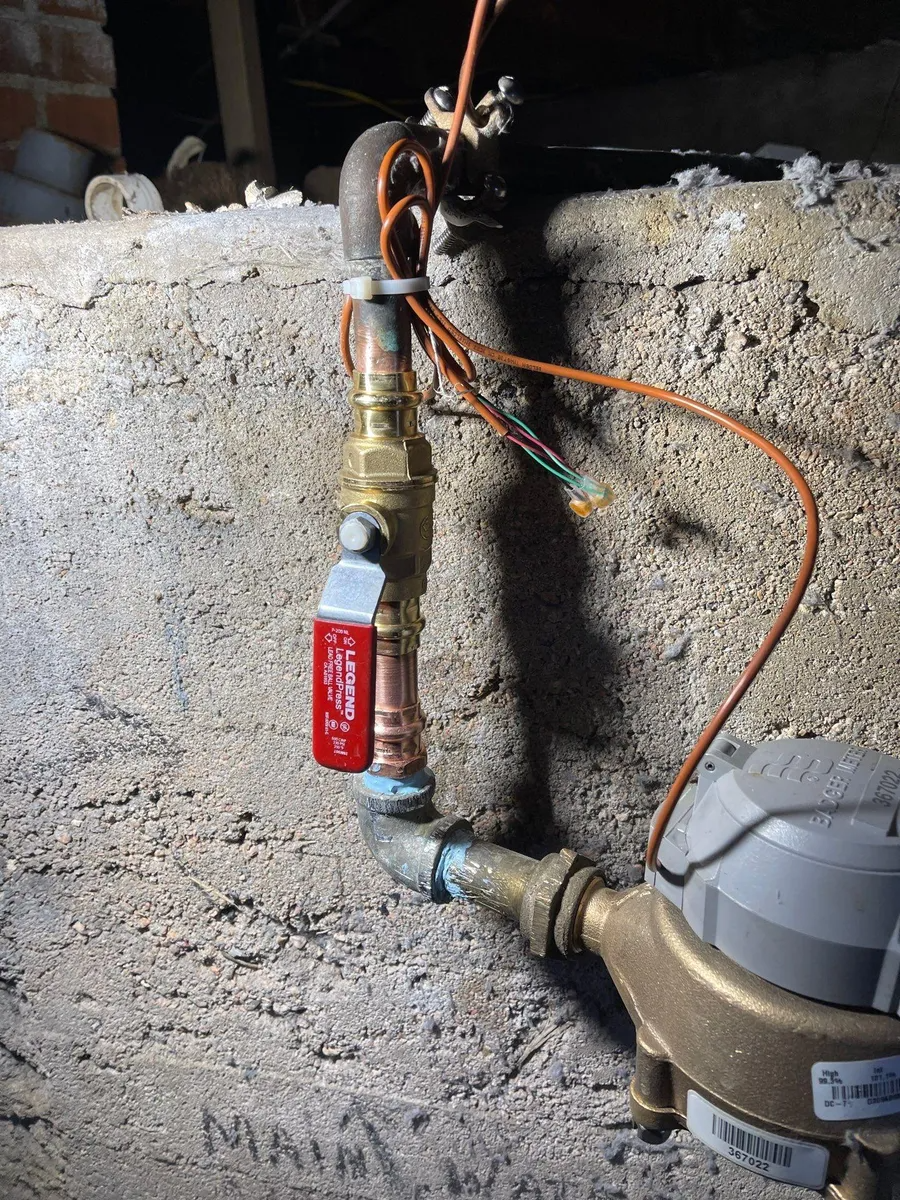 Water pipe with red shutoff valve and exposed wiring against a concrete wall