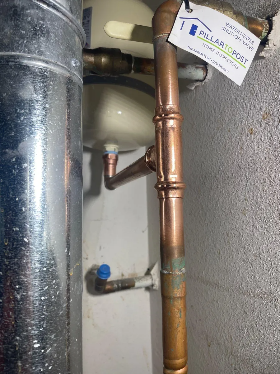 Copper plumbing pipes with valves and a blue cap in a utility closet