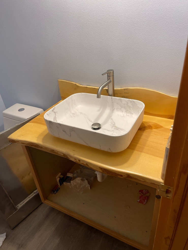 Bathroom sink on a wooden counter with a gray wall and toilet beside it.