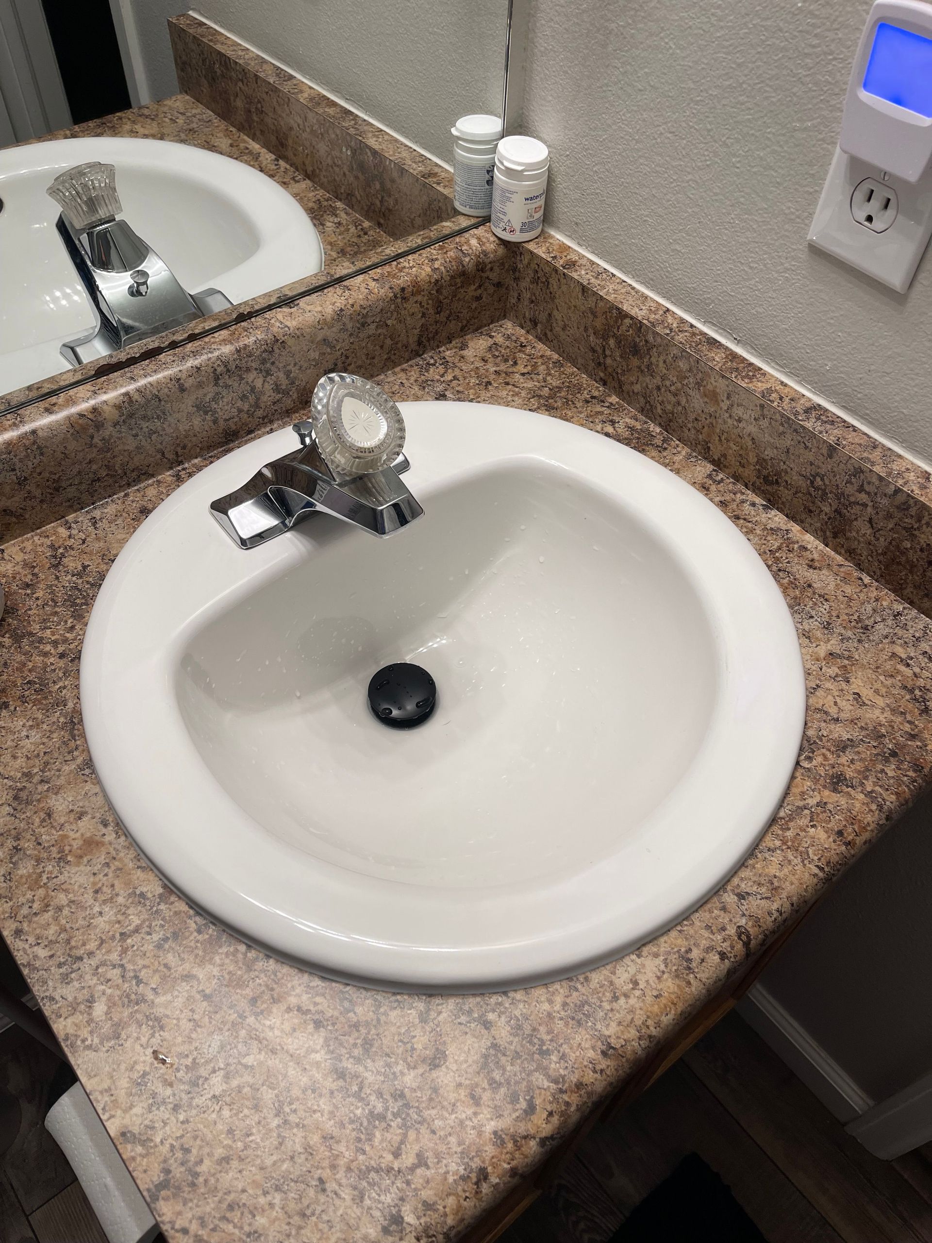Bathroom sink with white basin, chrome faucet, and speckled countertop beneath a wall mirror.