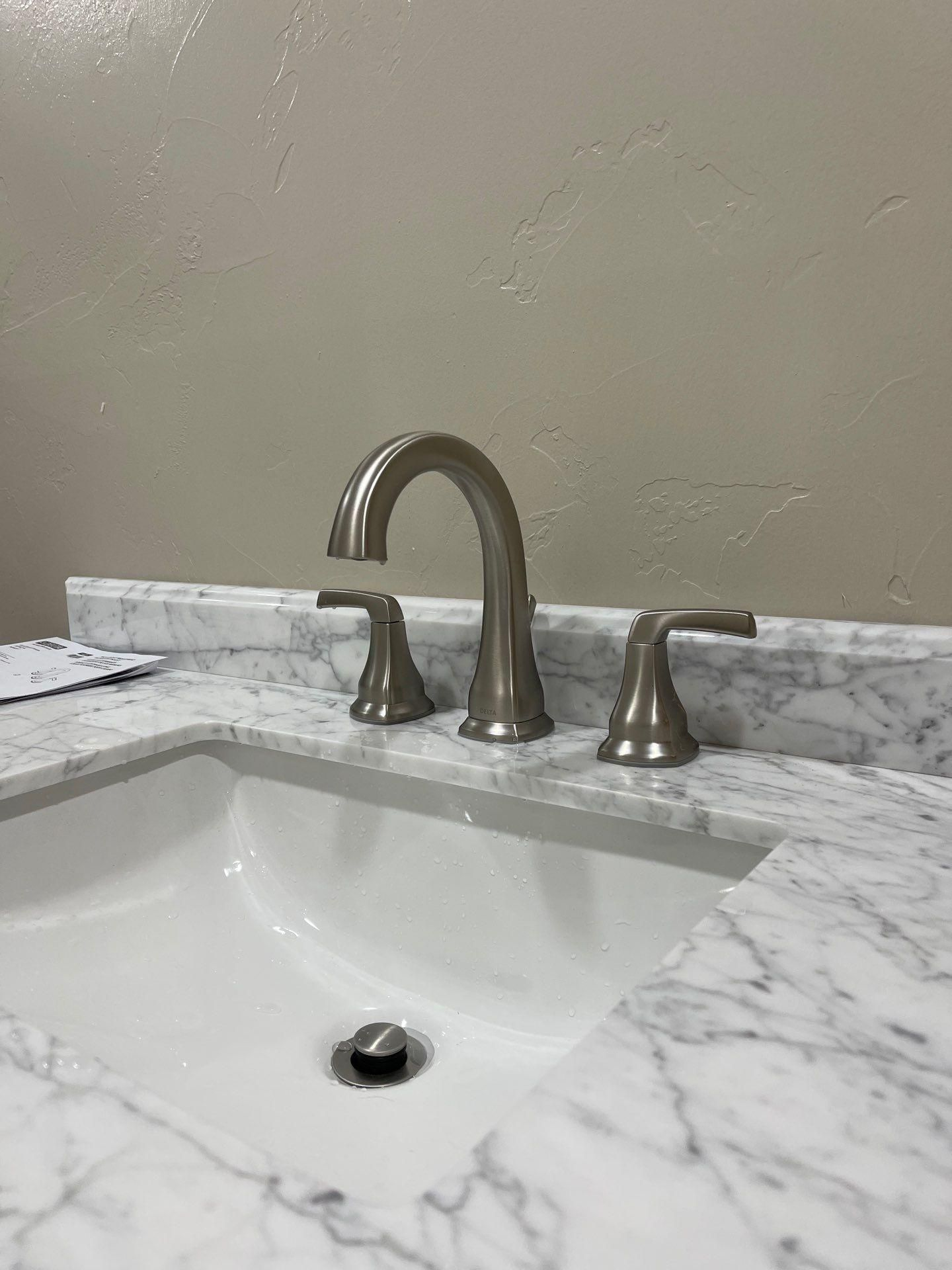 White marble bathroom sink with brushed-nickel faucet and beige wall behind it