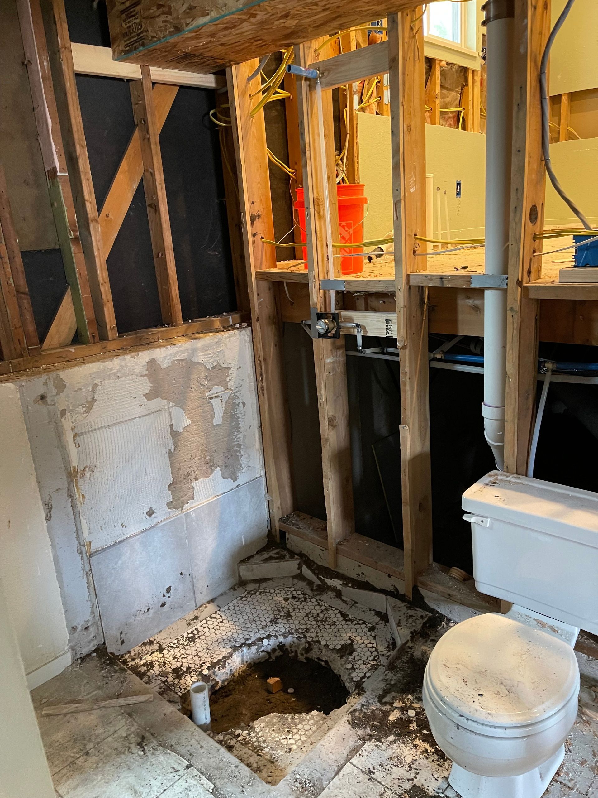 Partially demolished bathroom with exposed studs, toilet, and a hole in the floor