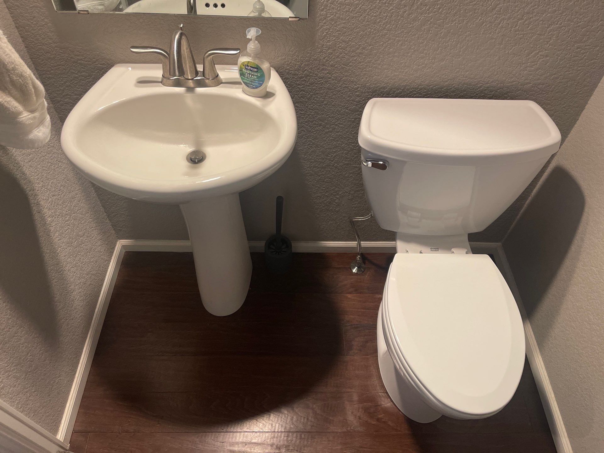 Small bathroom with pedestal sink, toilet, and dark wood floor.