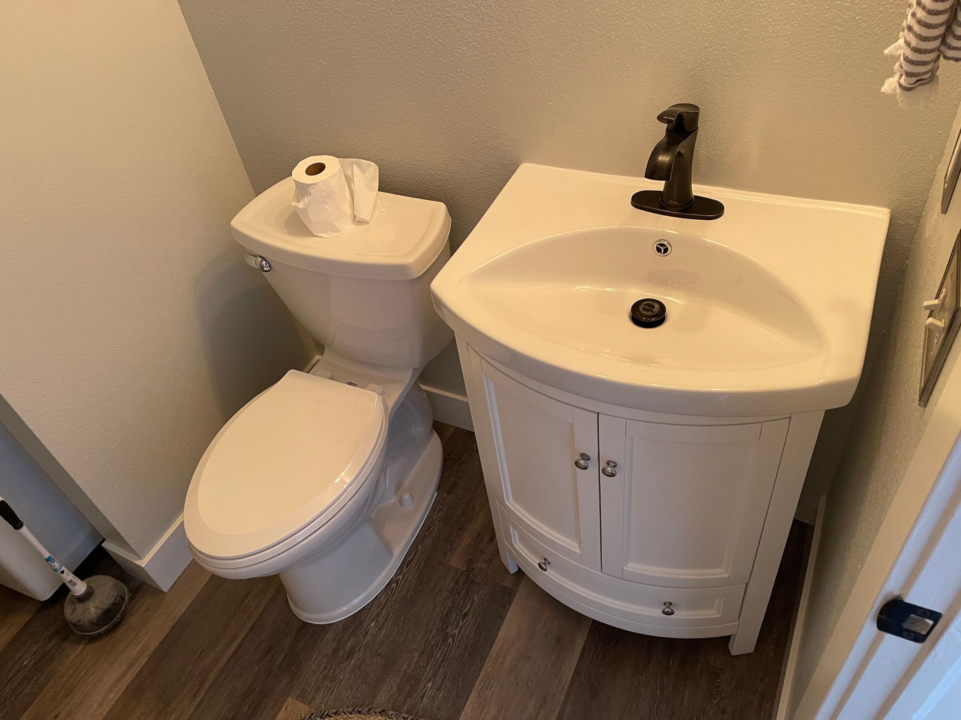 Small bathroom with toilet and white sink vanity on wood-look floor.