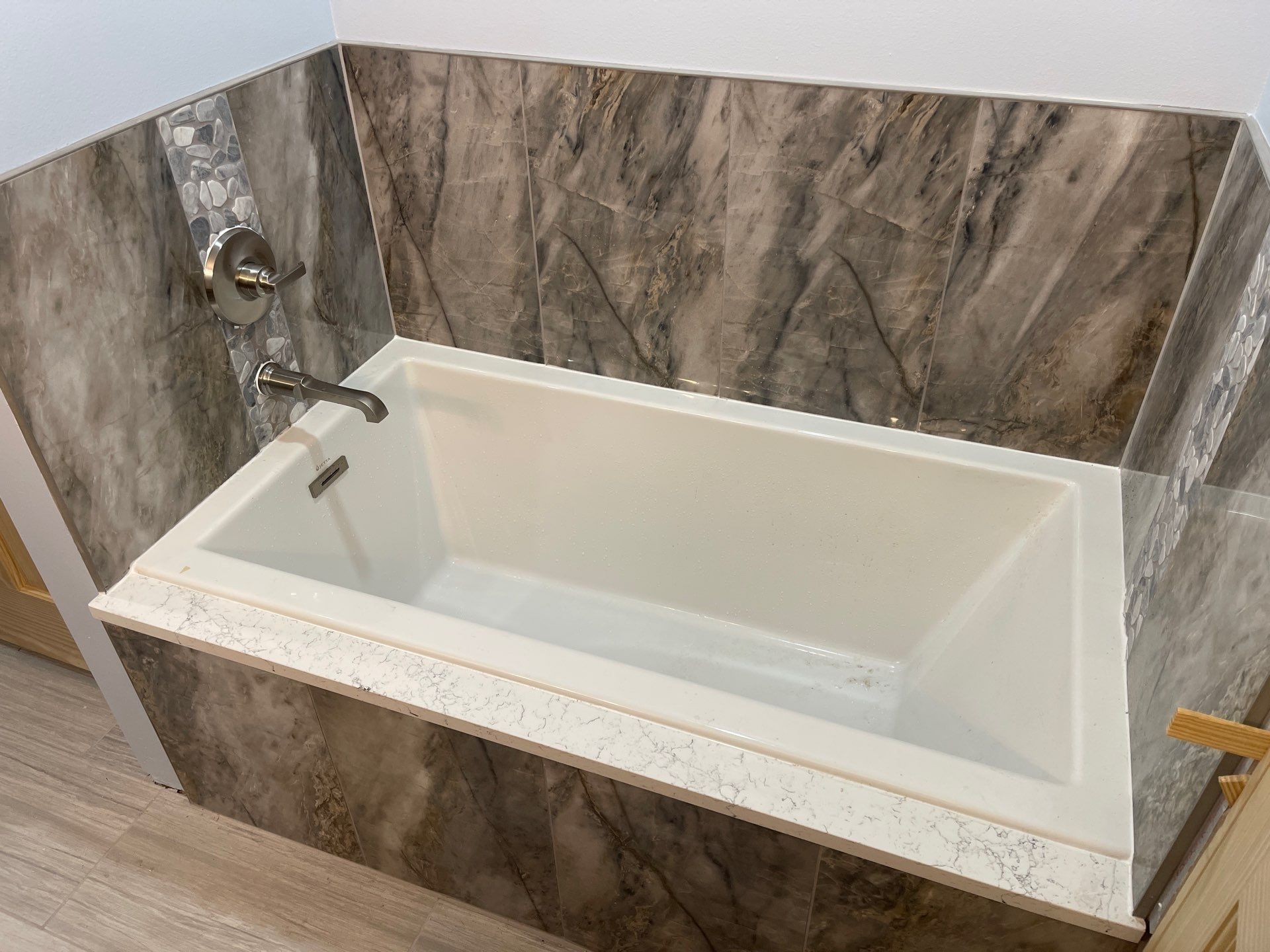 White rectangular bathtub with chrome faucet and marble-look tile surround in a bathroom