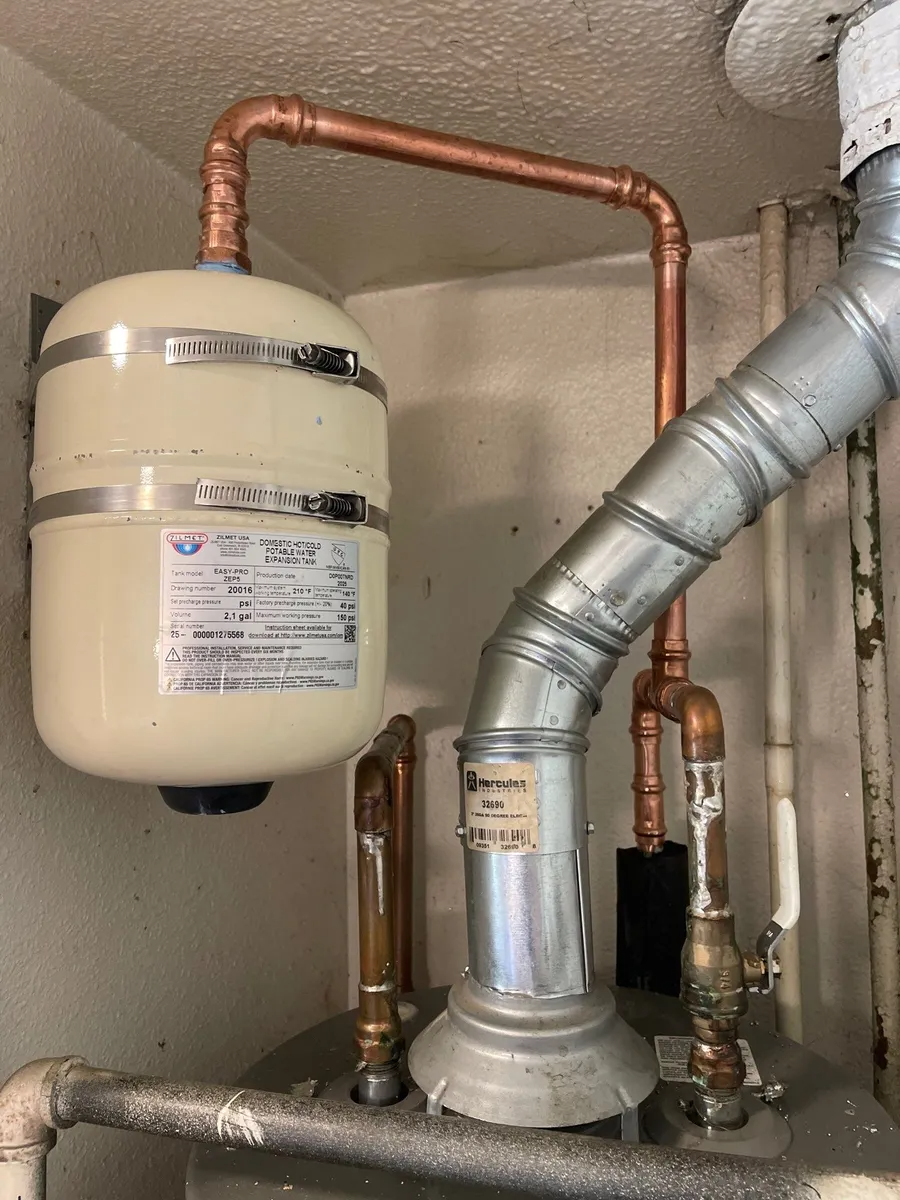 Indoor utility room with copper piping, a white expansion tank, and a metal flue vent.