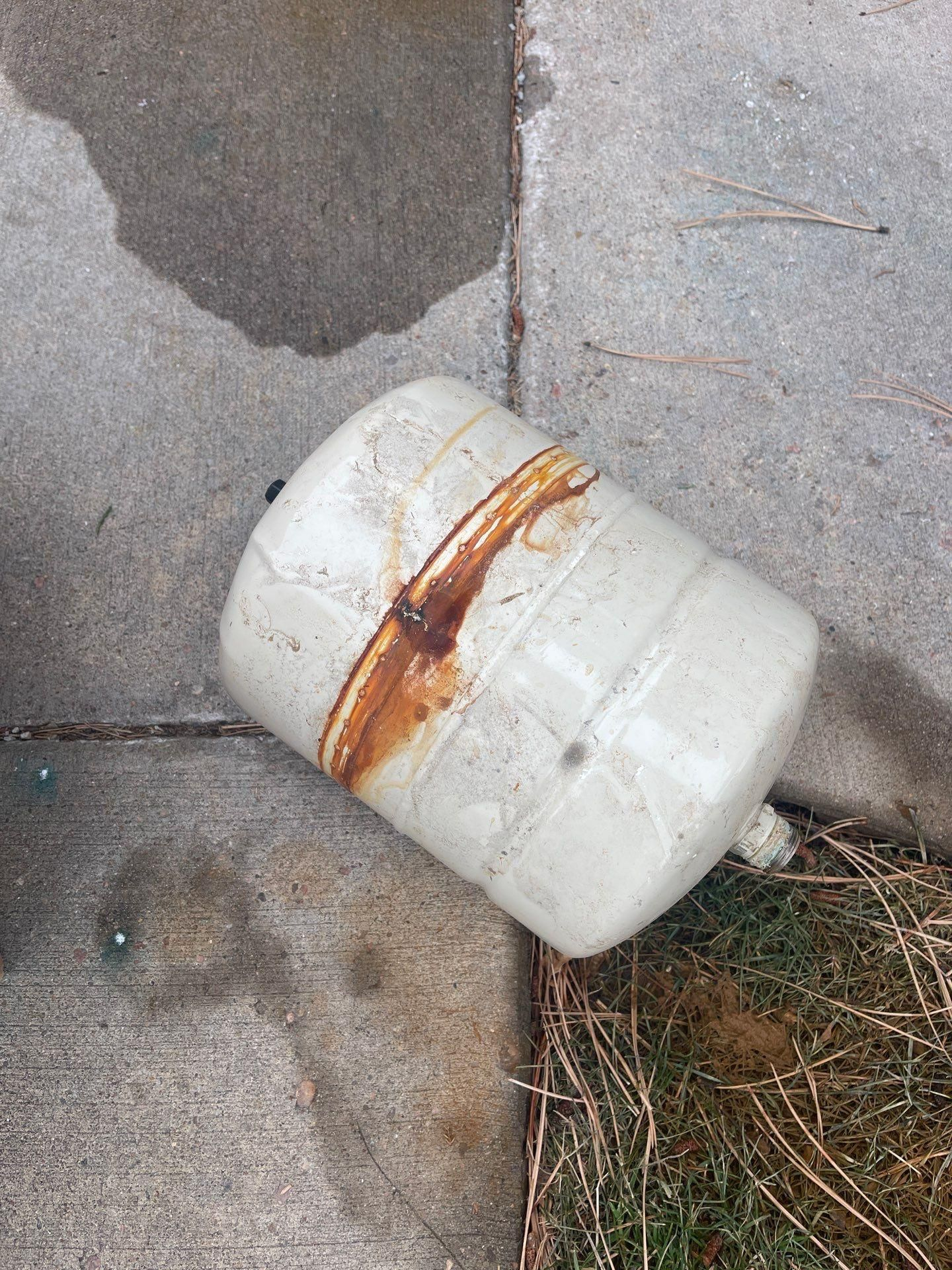 White plastic bucket with orange rust stain lying on a concrete sidewalk near grass.