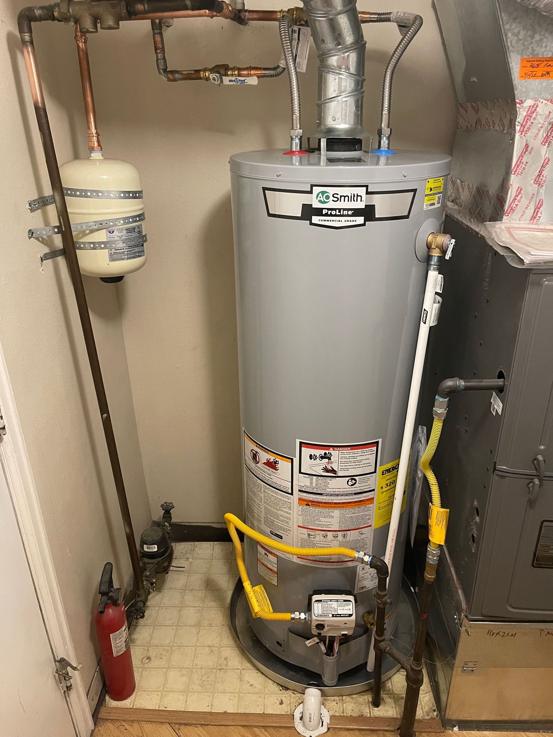 Water heater in a utility closet with copper pipes, a red fire extinguisher, and a yellow gas line protector.