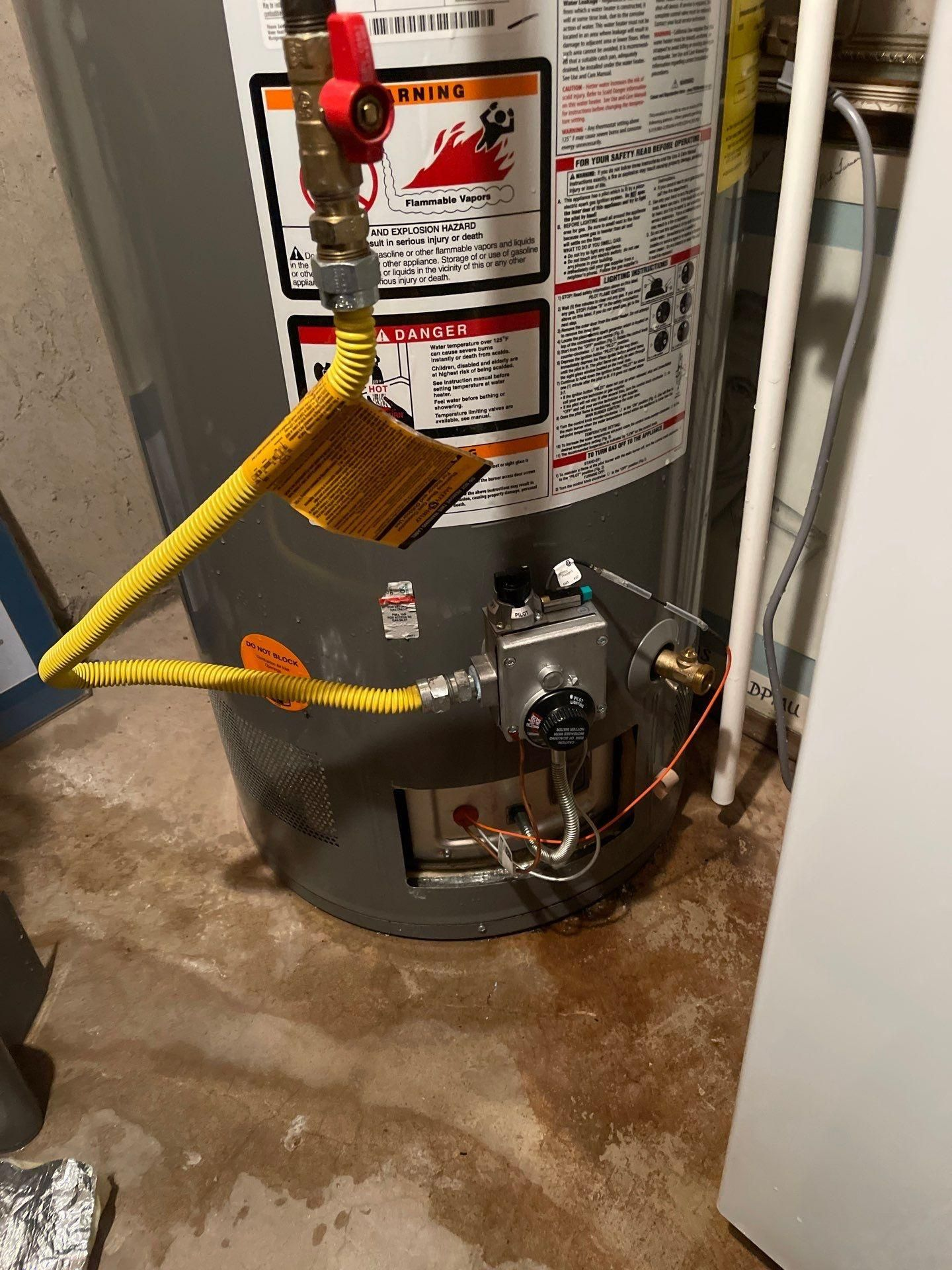 Water heater with yellow gas line and control valve in a utility closet, with water on the floor