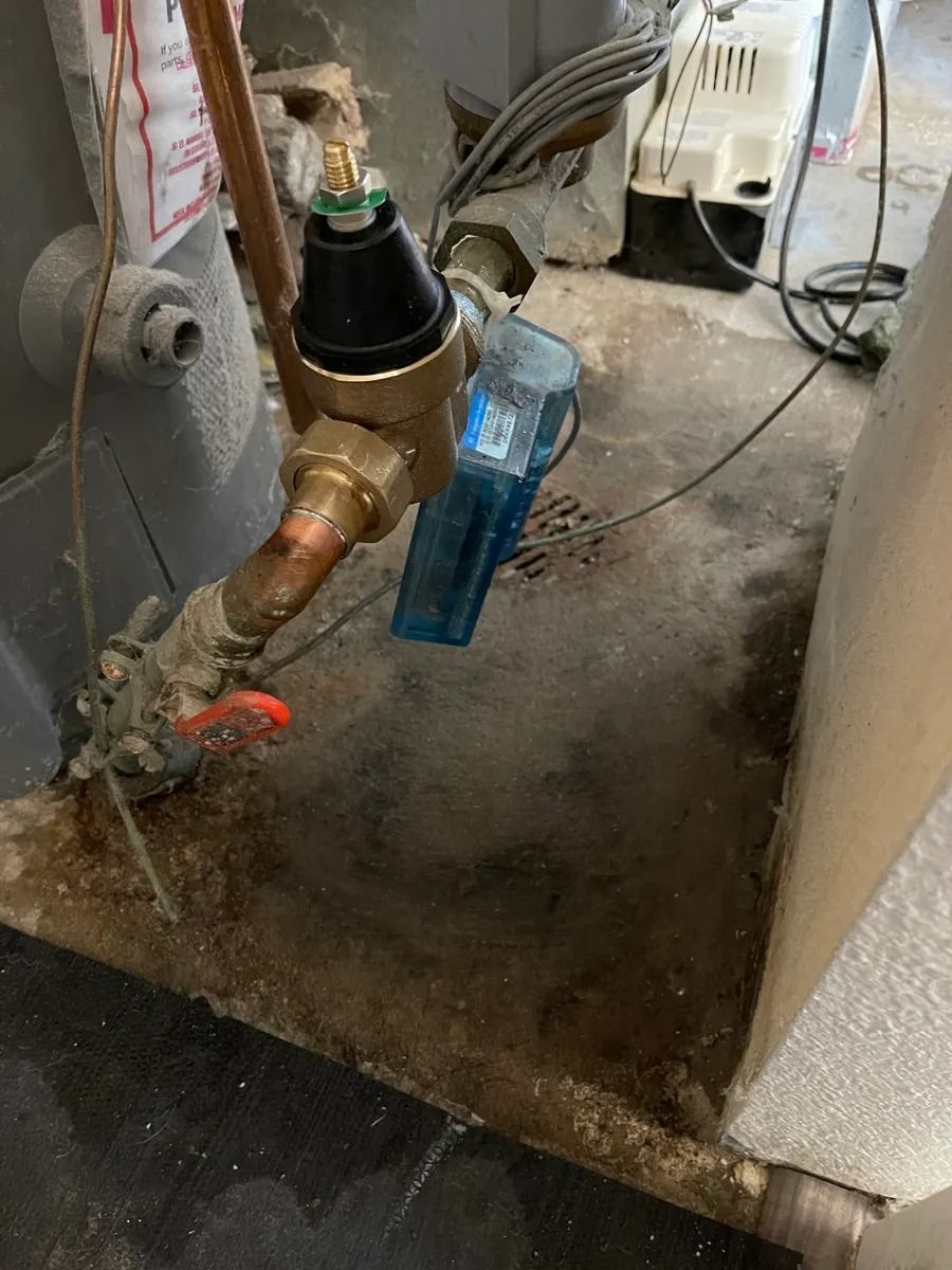 Close-up of a brass water valve and blue filter attachment in a utility area with dirty floor.