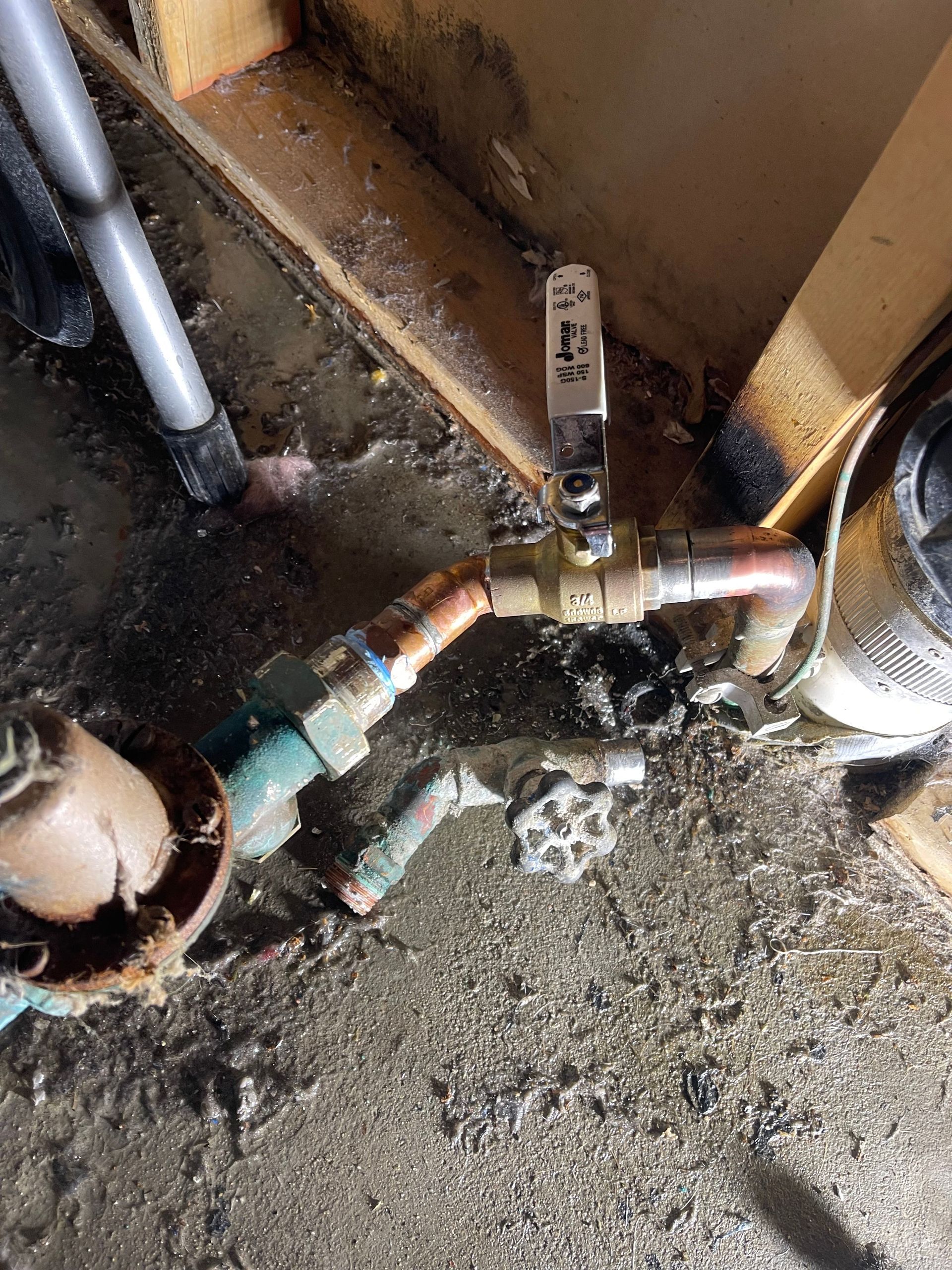 Leaking water pipe and valve near a wall on a wet, dirty floor.