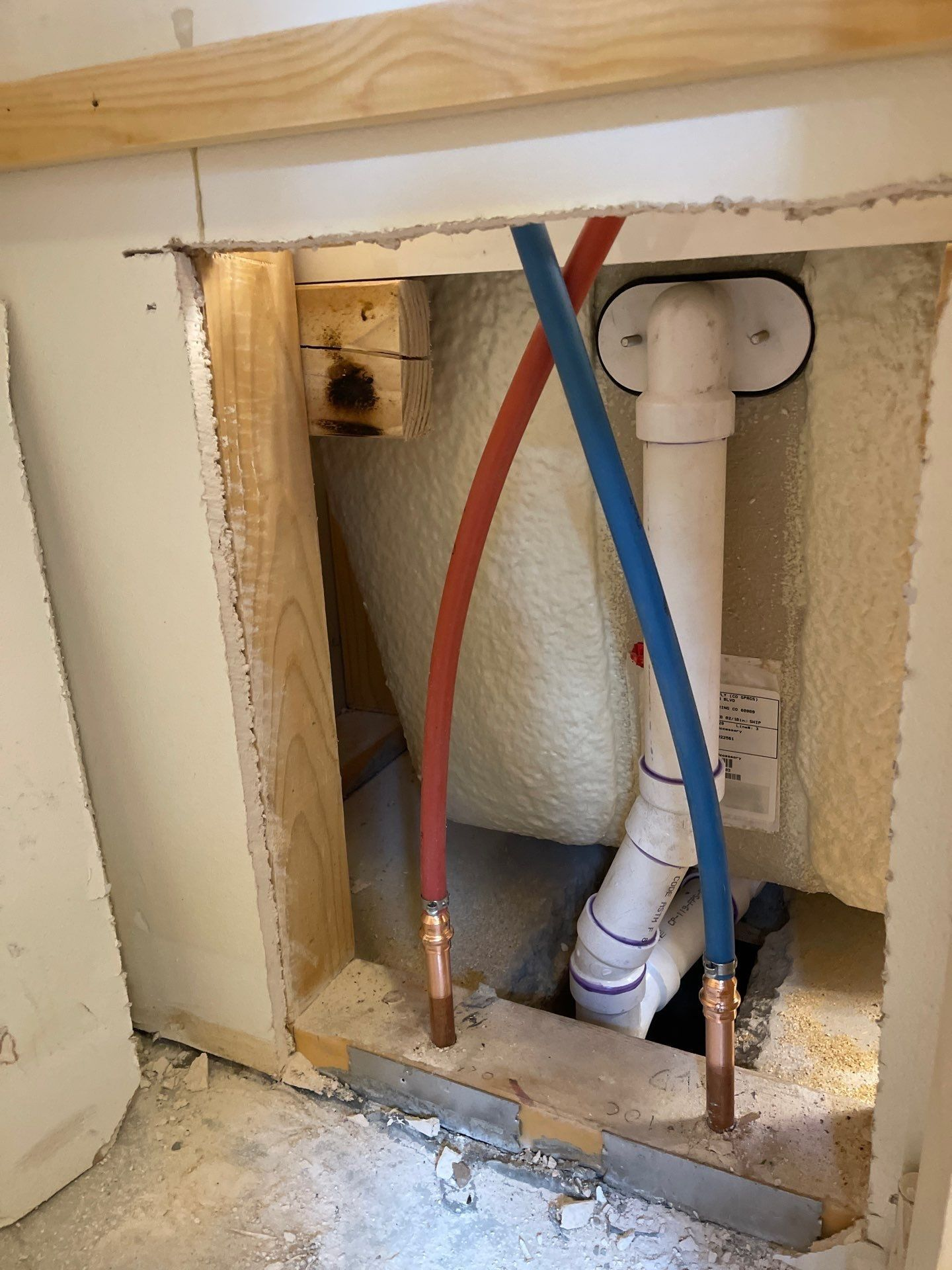Open wall with plumbing pipes and red and blue supply lines in a bathroom or utility area