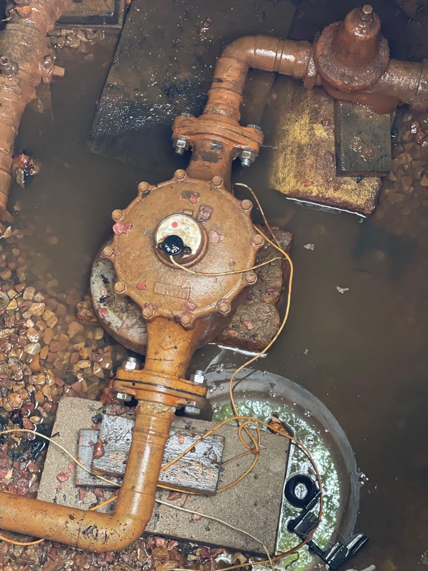 Rusty underground water valve and pipes in a muddy utility pit