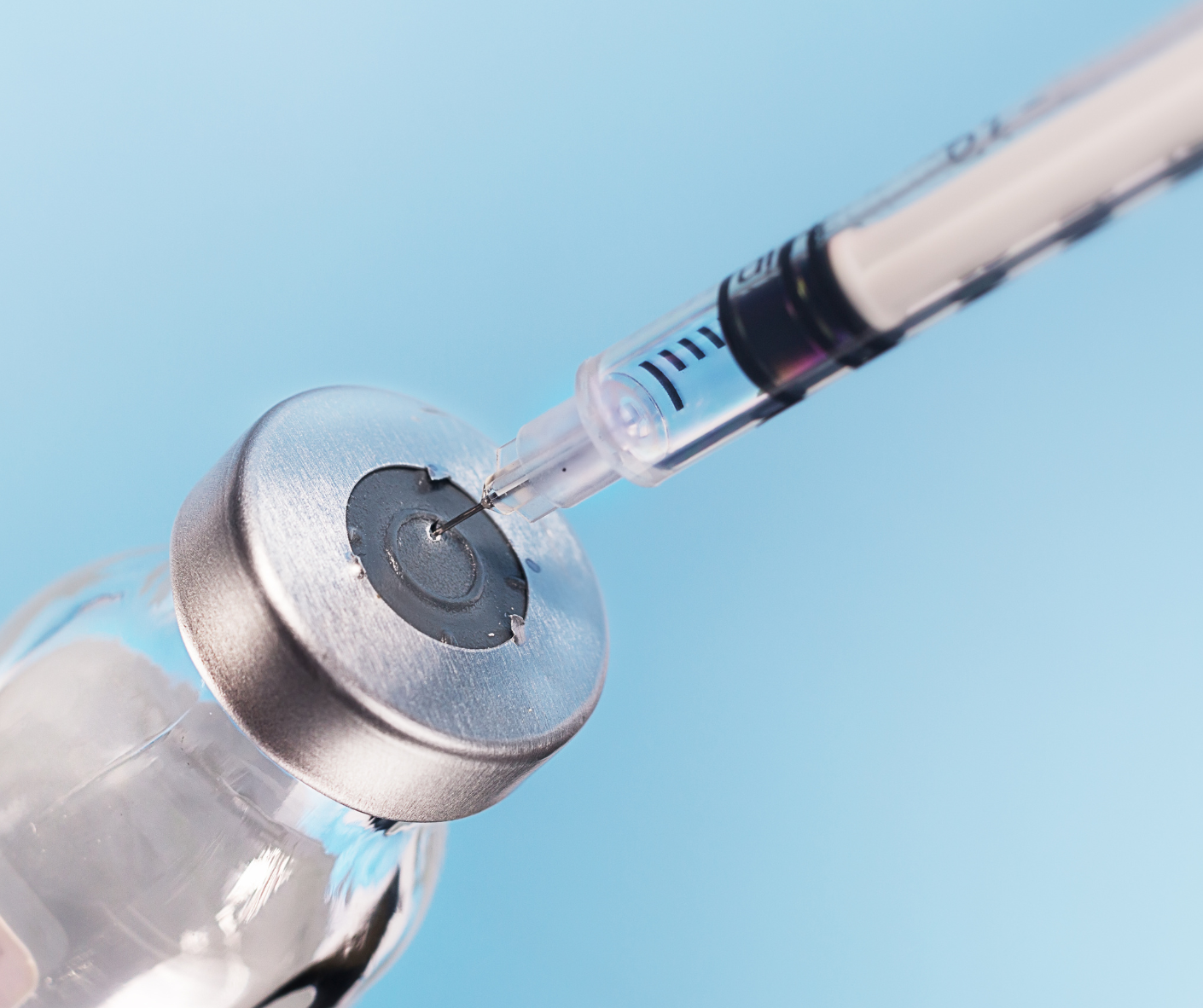 Syringe injecting clear liquid from a vial with a metal cap, on blue background.
