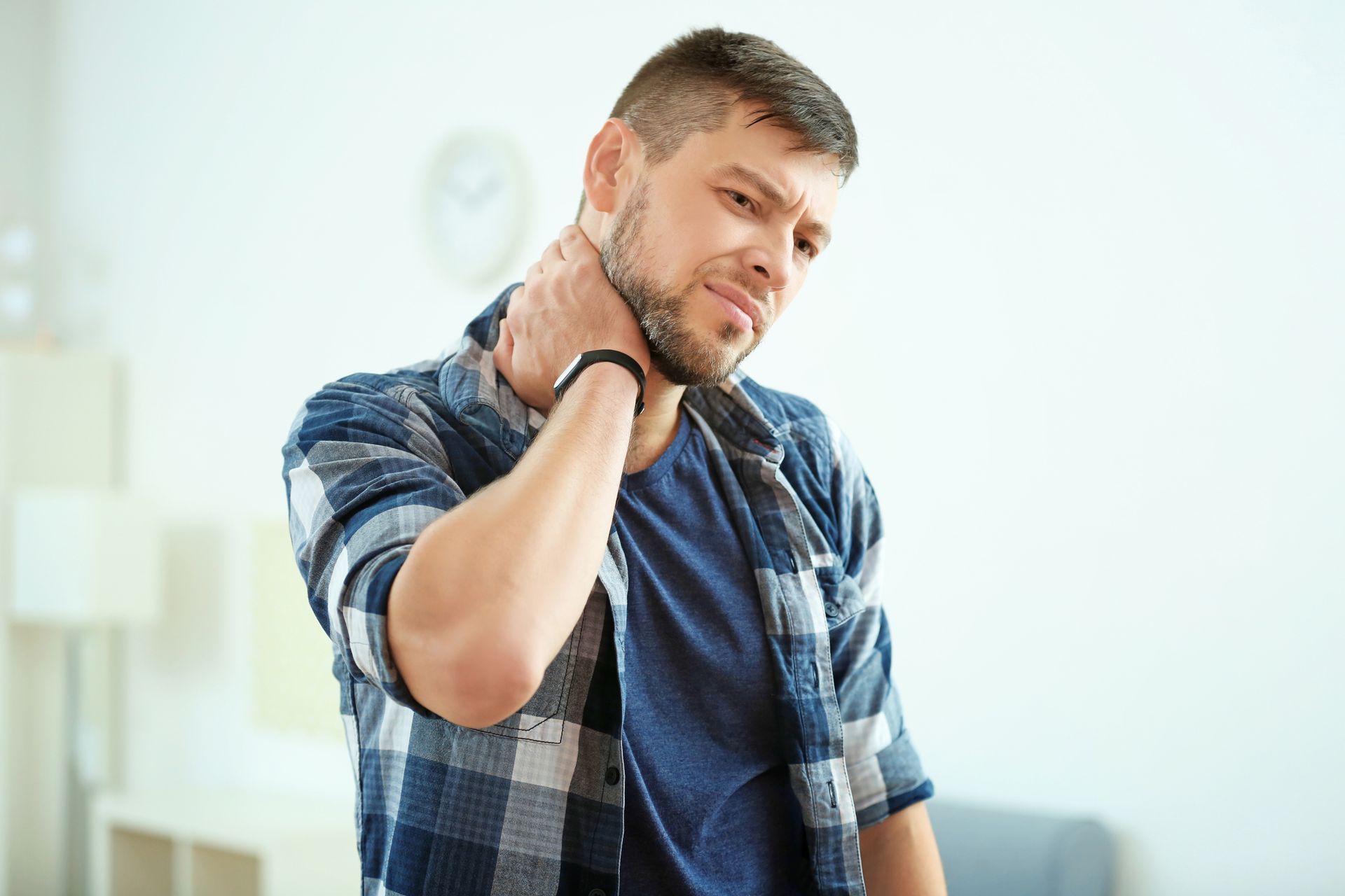 A man is holding his neck in pain while sitting on a couch.