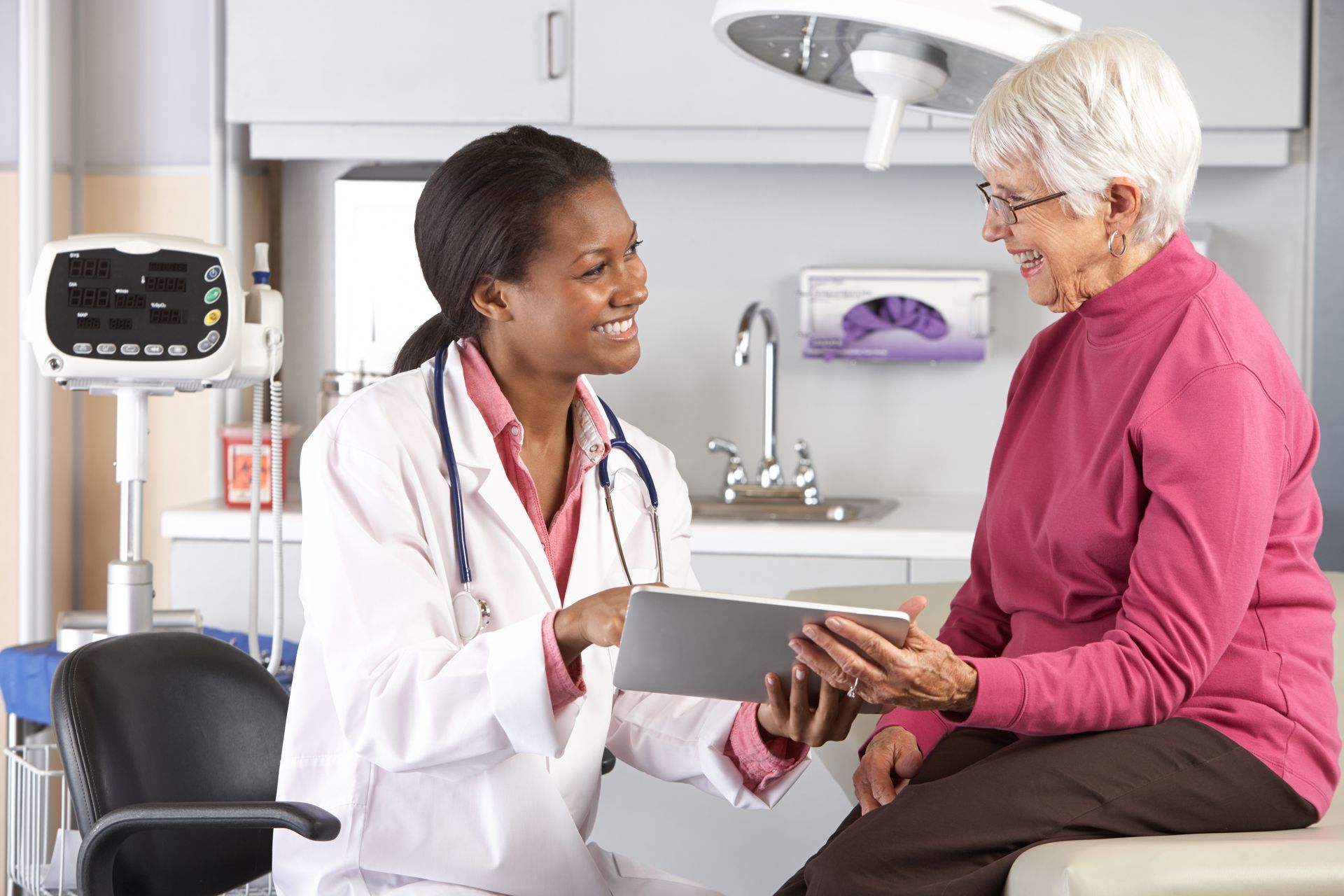 A doctor is talking to an elderly woman while holding a tablet.