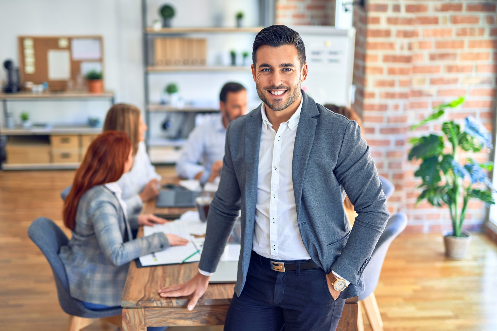 A man in a suit is standing in front of a group of people in an office.