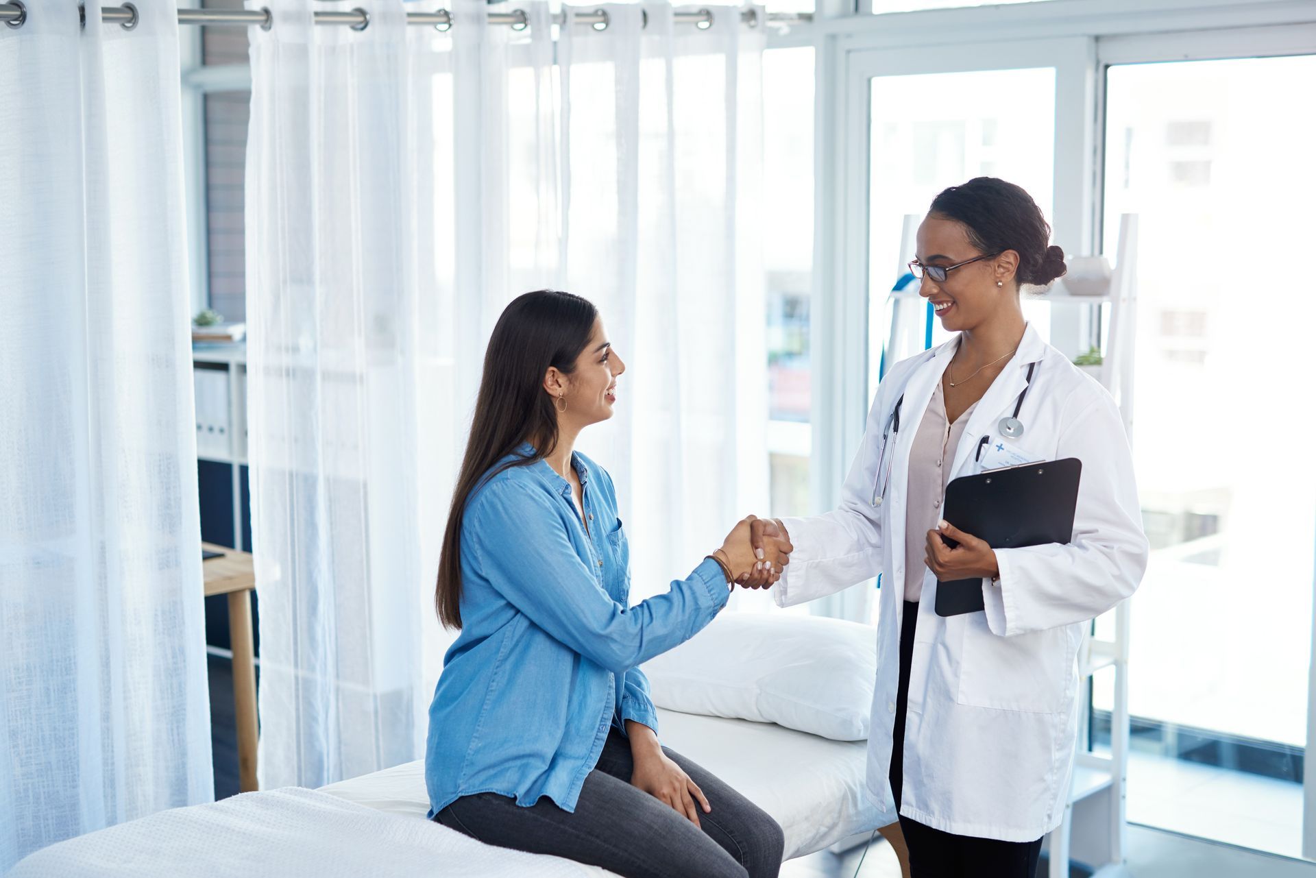 A pregnant woman is sitting on a bed shaking hands with a doctor.