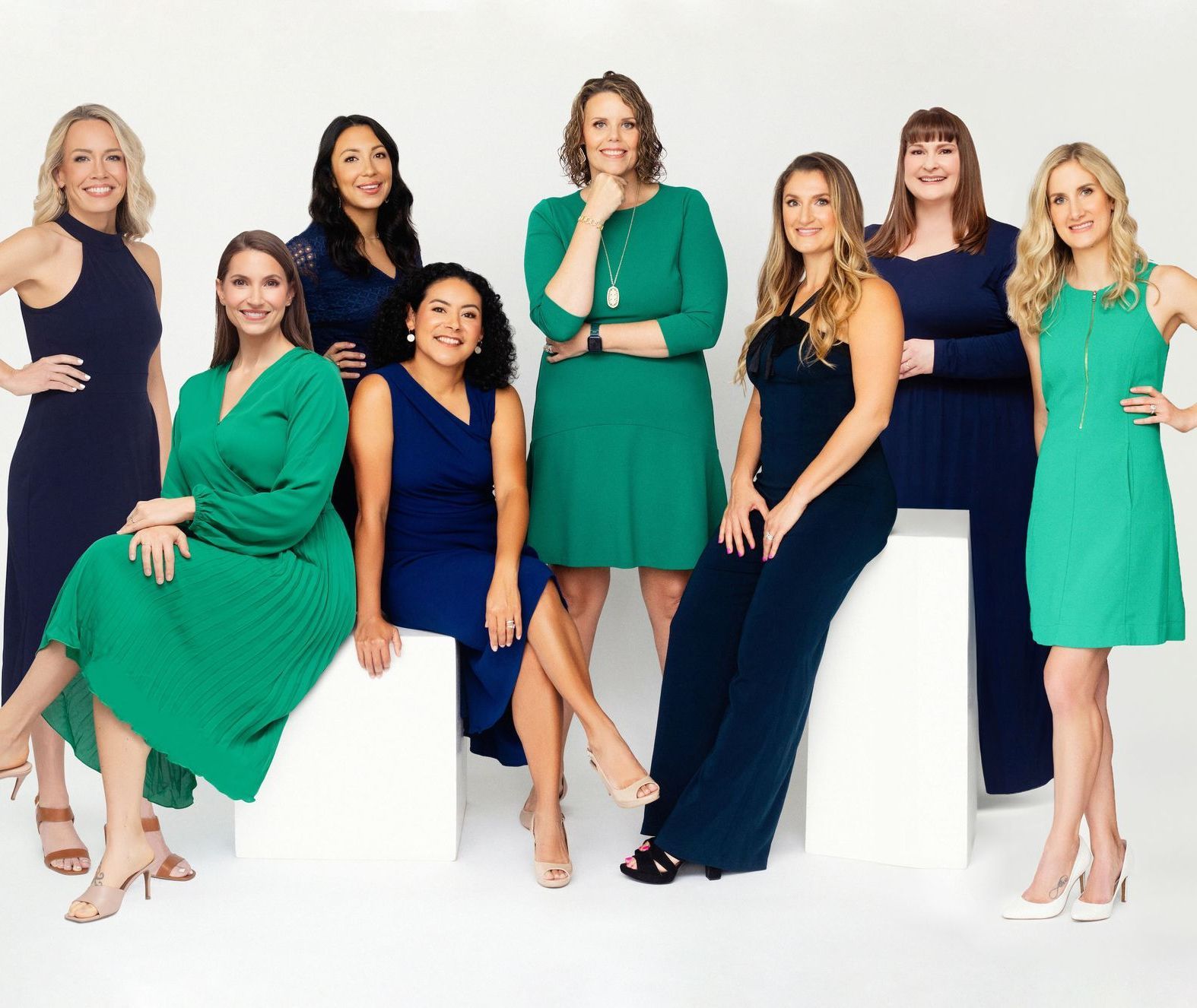 Eight women in blue and green dresses are posing for a picture