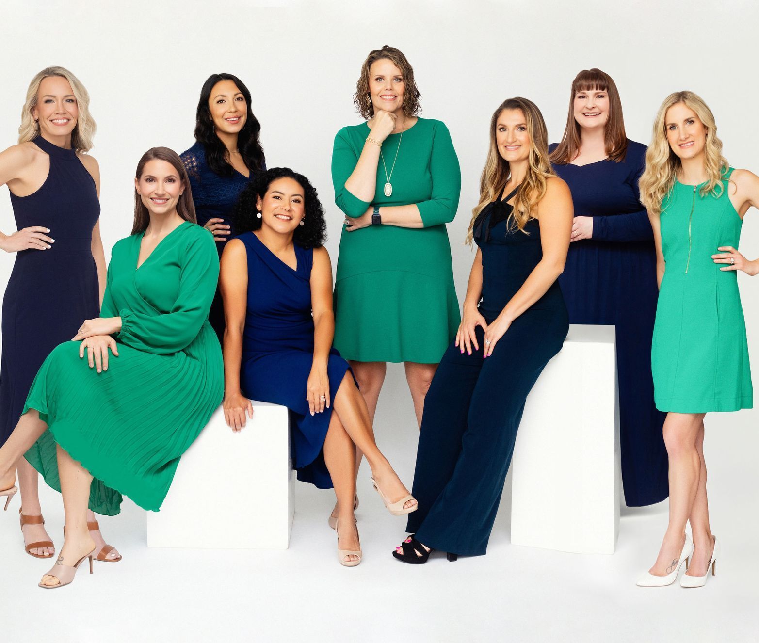 Eight women in blue and green dresses are posing for a picture