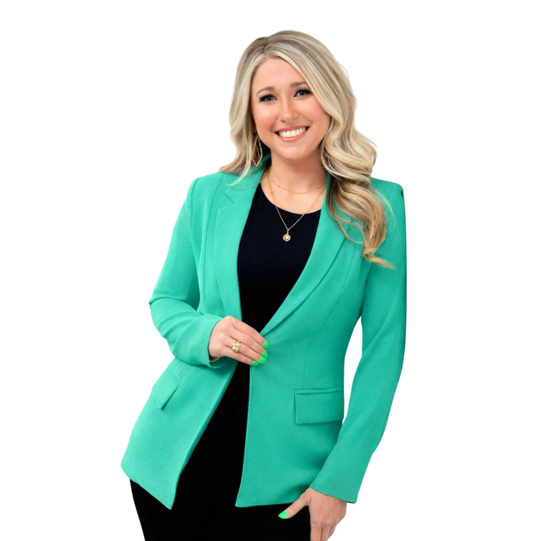 Woman in green blazer and black shirt, smiling, posing with hands on blazer.