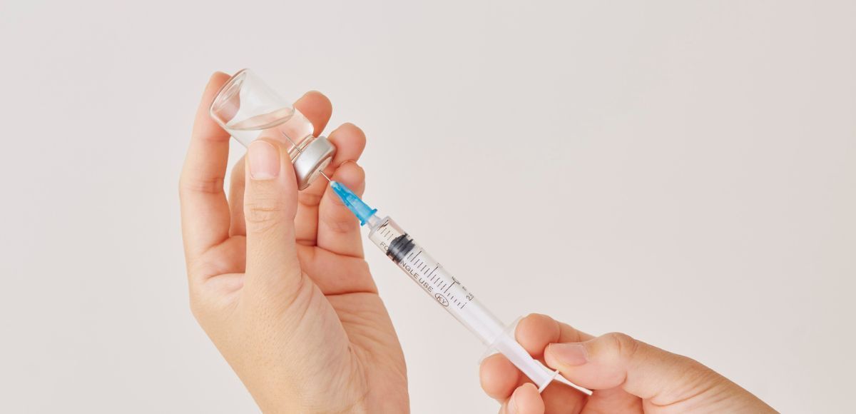 Hands drawing medicine from a vial into a syringe on a white background