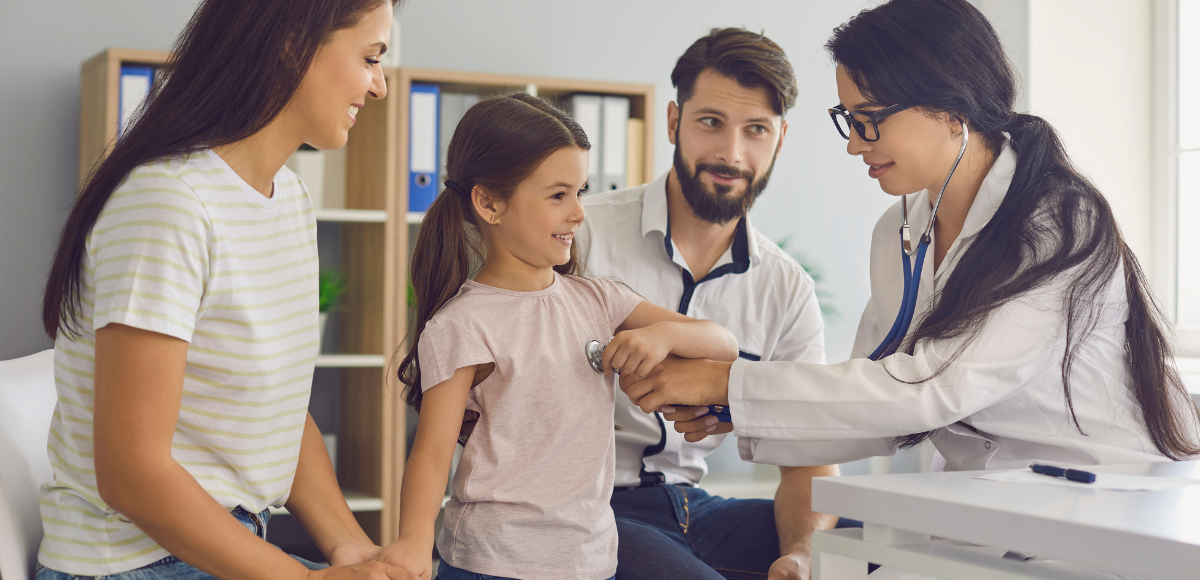 A doctor uses a stethoscope to examine a young girl while her parents watch in a clinic office.