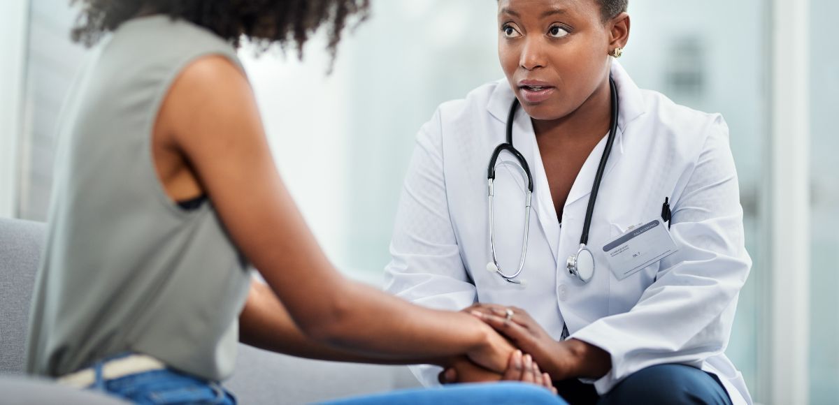 Doctor speaking with a patient in a clinic, holding the patient’s hands reassuringly.