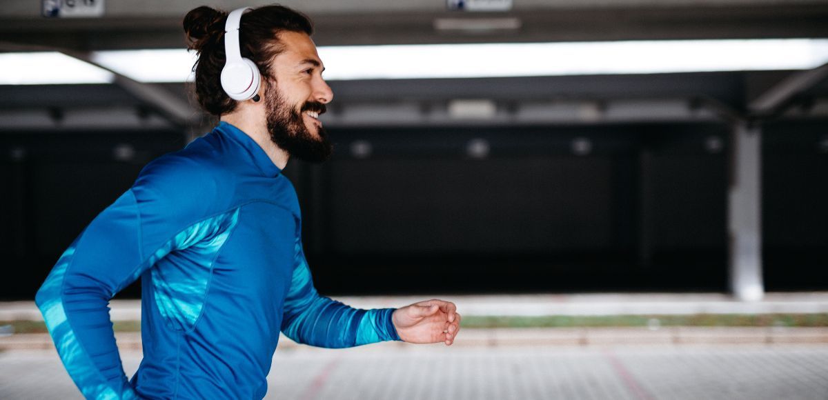 Man jogging indoors wearing white headphones and a blue jacket