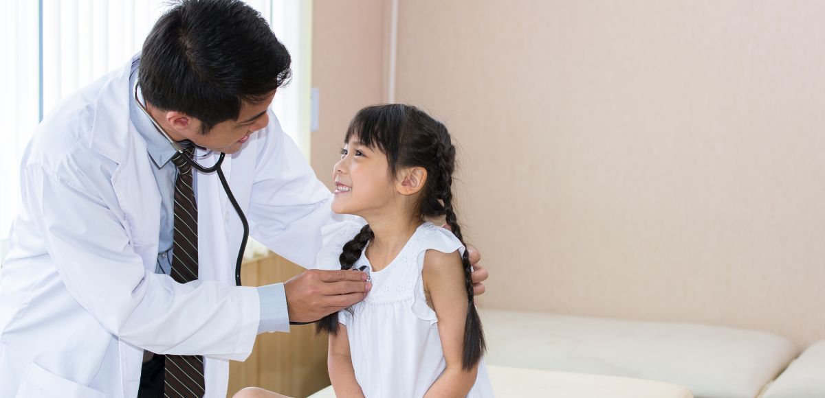 Doctor examining a smiling child in a clinic with a stethoscope