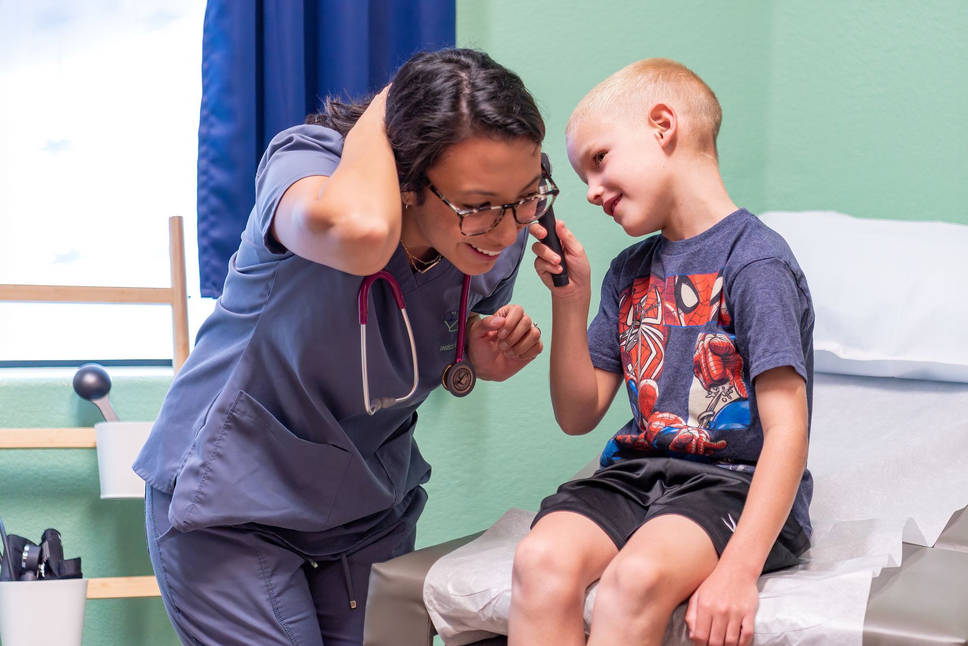 A nurse is examining a young boy 's ear with a stethoscope.
