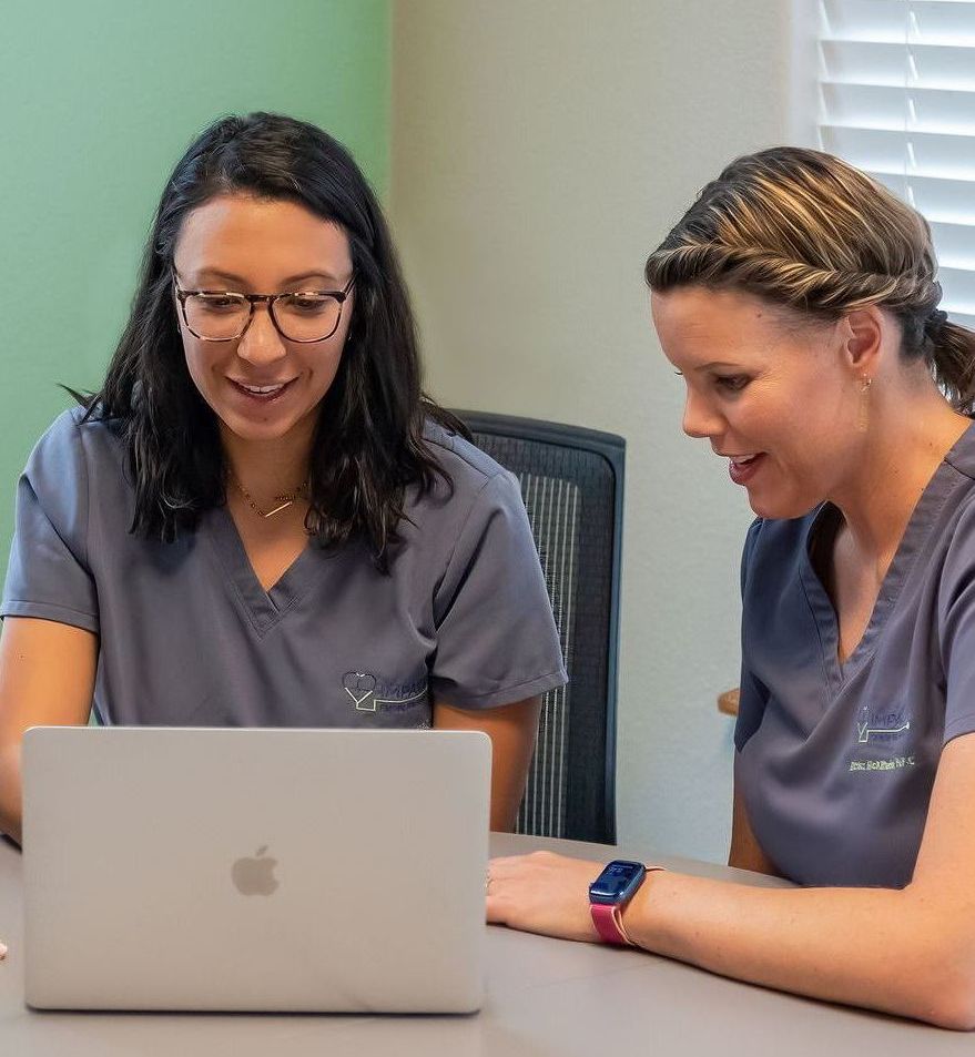 Two women are sitting at a table looking at a laptop computer.