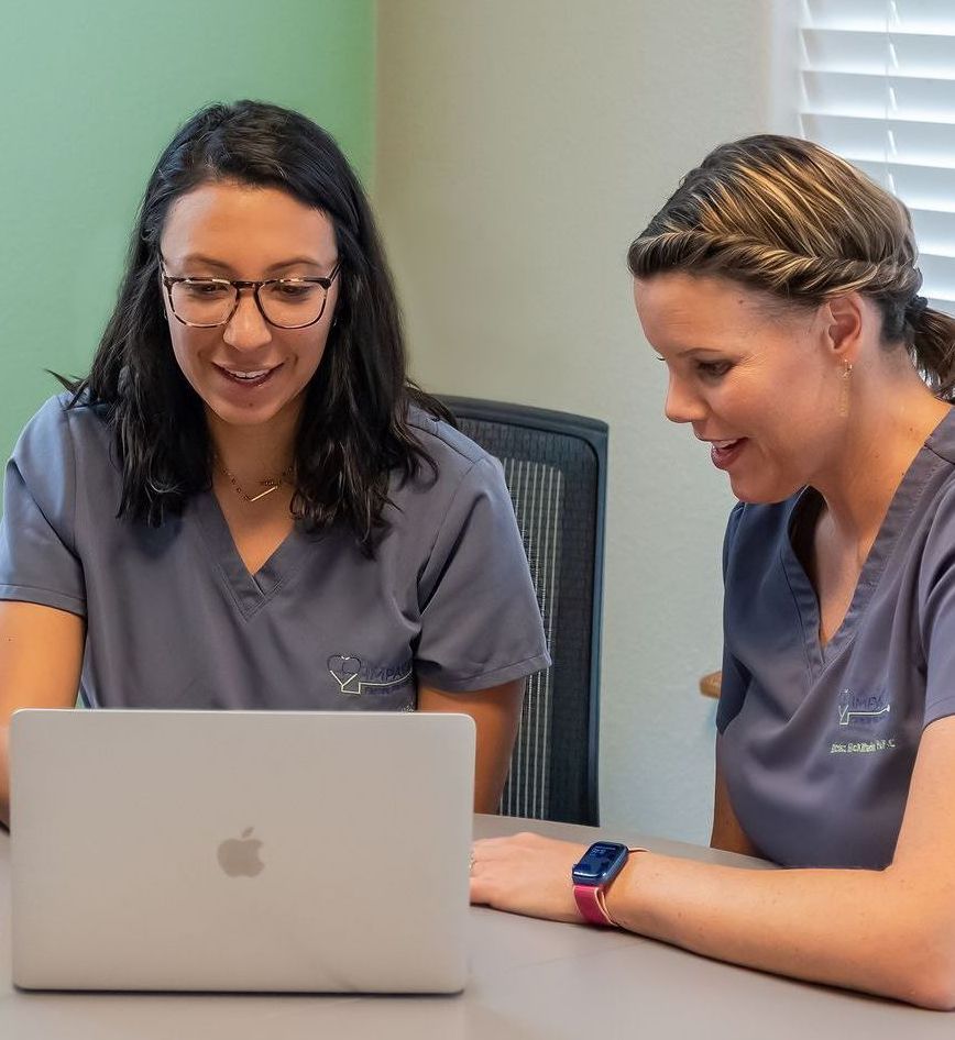 Two women are sitting at a table looking at a laptop computer.