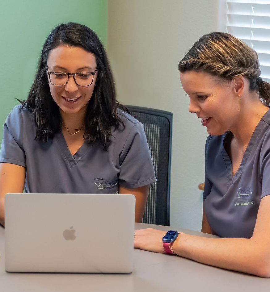 Two women are sitting at a table looking at a laptop computer.