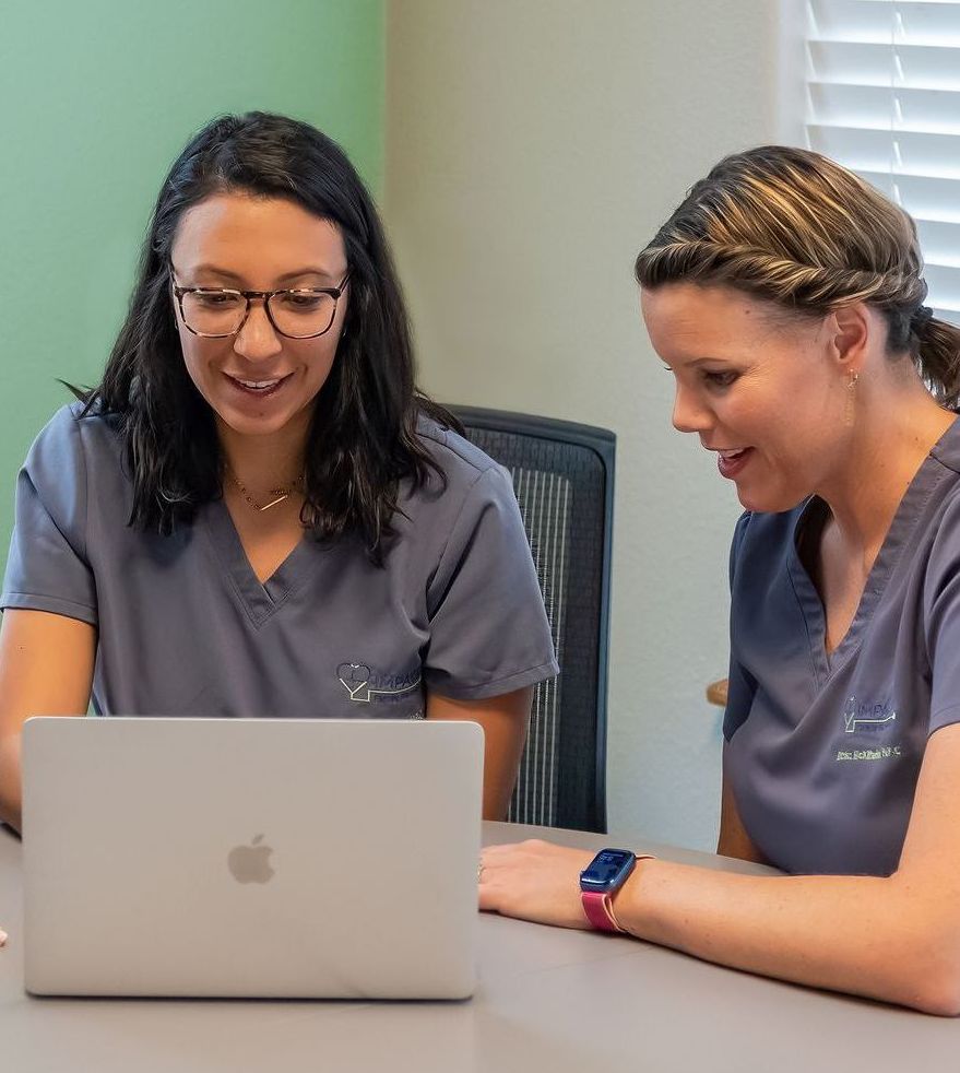 Two women are sitting at a table looking at a laptop computer.