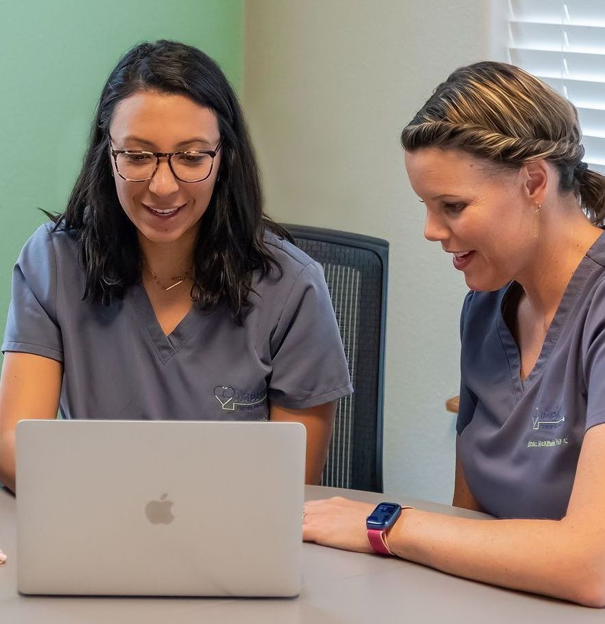 Two women are sitting at a table looking at a laptop computer.