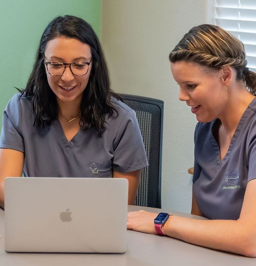 Two women are sitting at a table looking at a laptop computer.