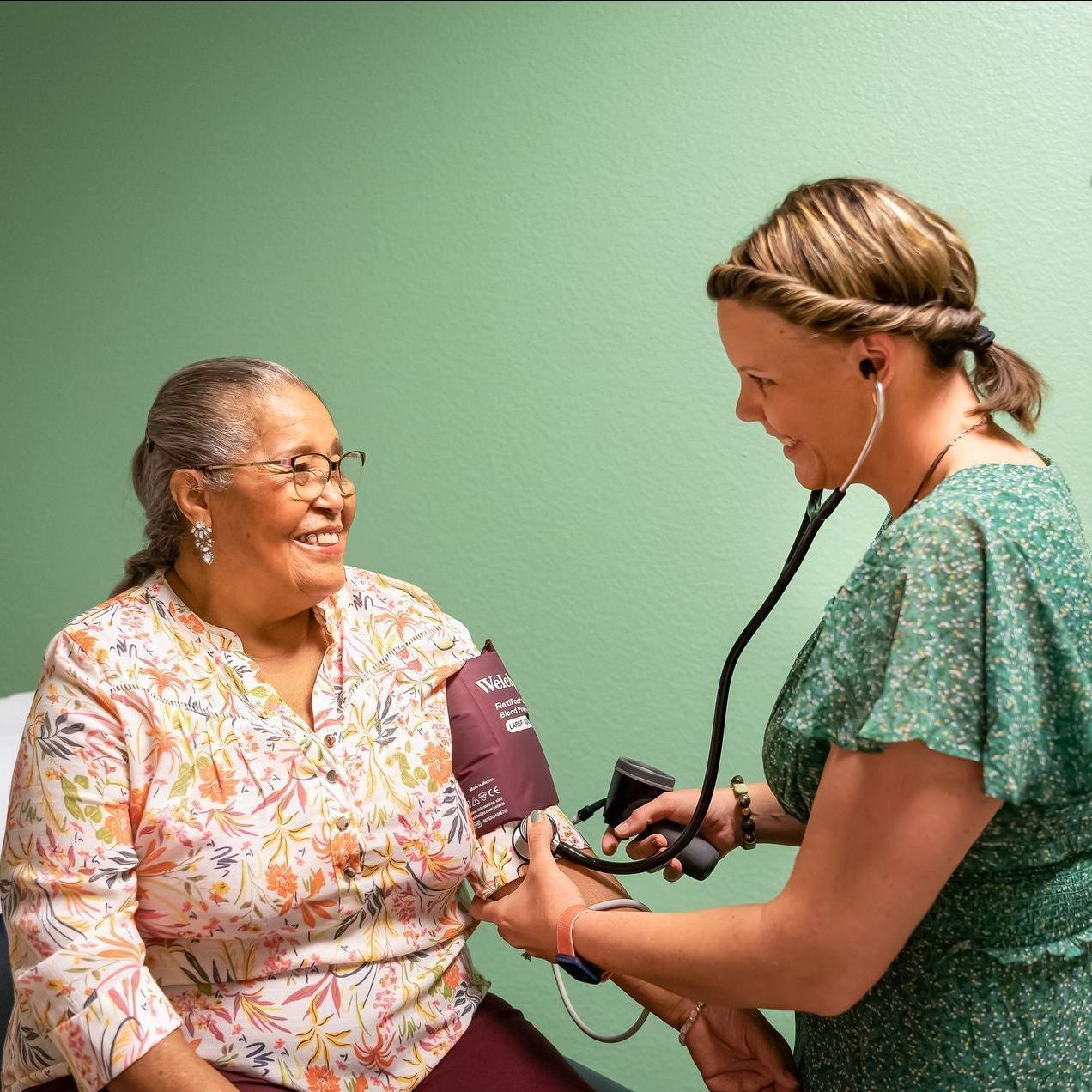 An older woman smiling as a healthcare professional checks her blood pressure