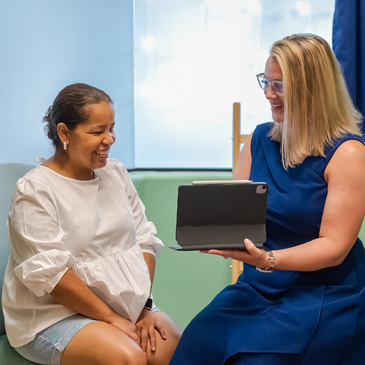 A pregnant woman is sitting next to a woman holding a laptop