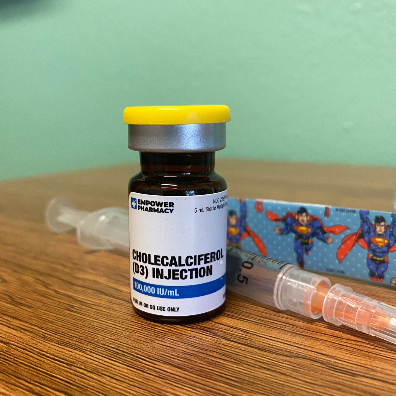A bottle of cholecalciferol injection is sitting on a wooden table next to a syringe.