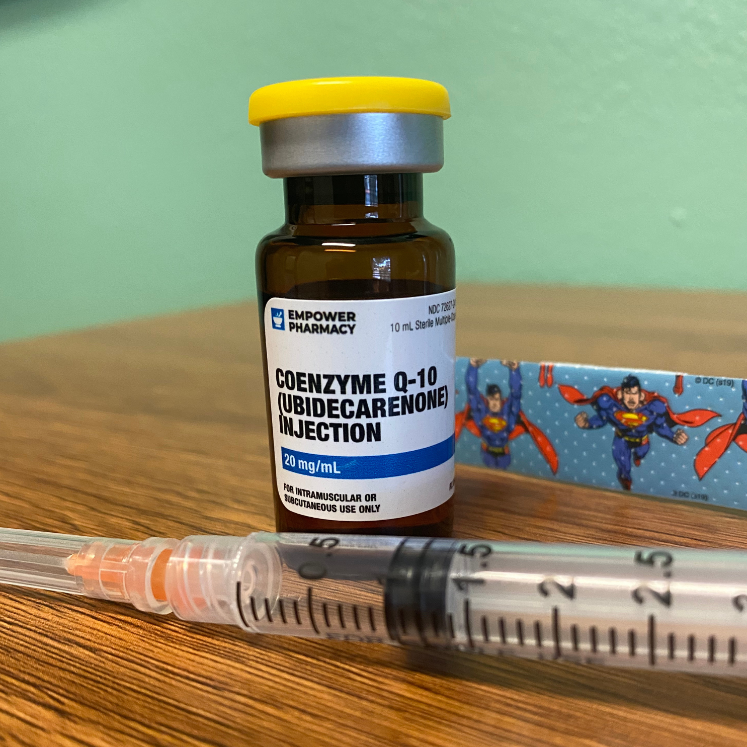 A bottle of coenzyme q10 ubidecarenone injection next to a syringe on a wooden table.