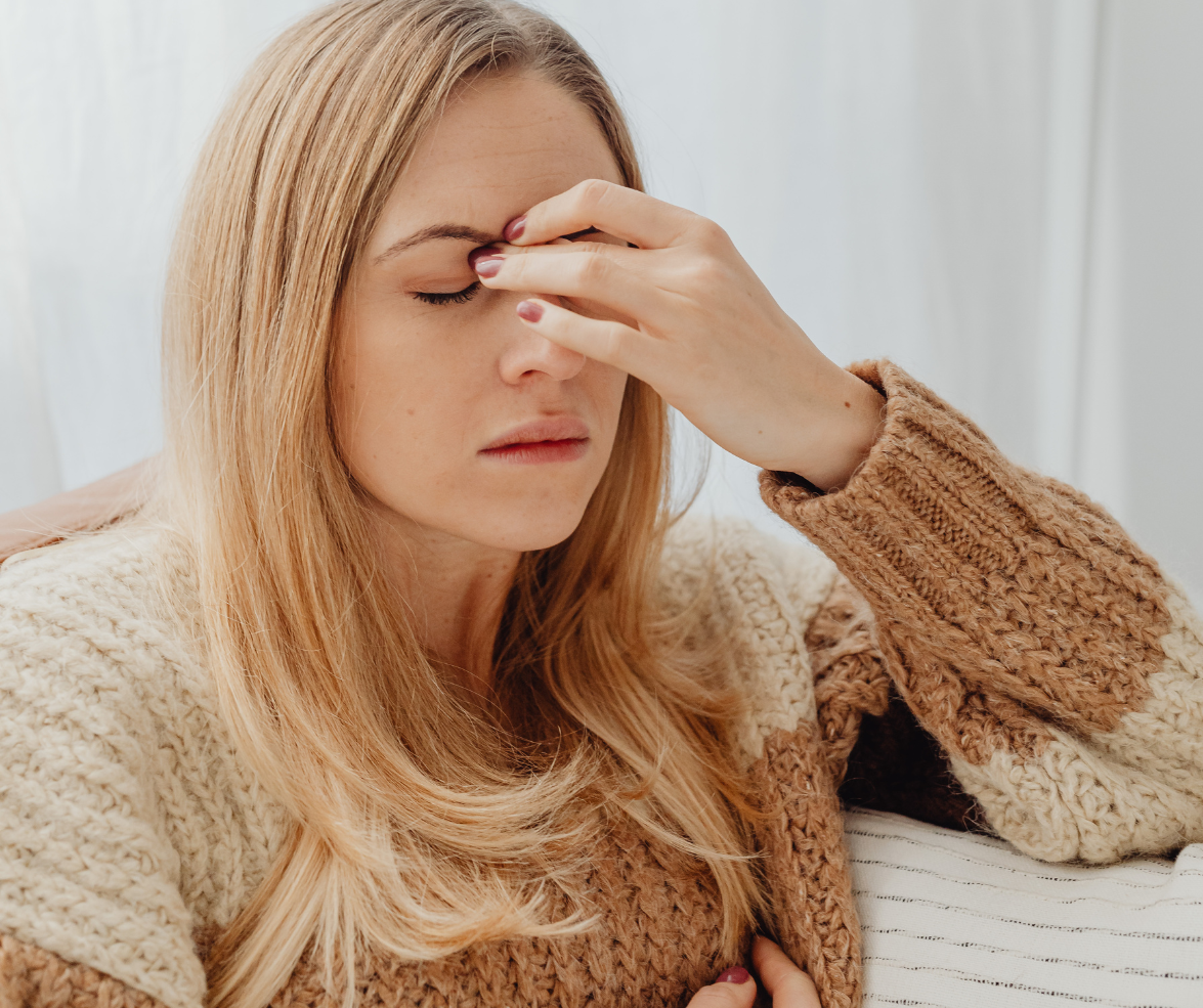 Woman with blonde hair touching forehead, possibly experiencing headache, wearing a sweater.