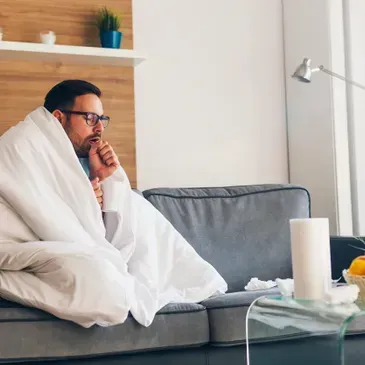 A man is sitting on a couch wrapped in a blanket.