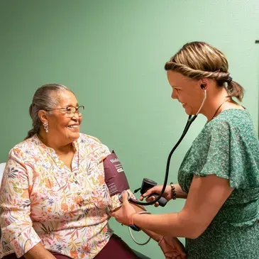 An older woman smiling as a healthcare professional checks her blood pressure