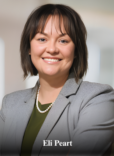 Woman in a grey blazer and pearl necklace smiles, arms crossed, with a blurred office background.