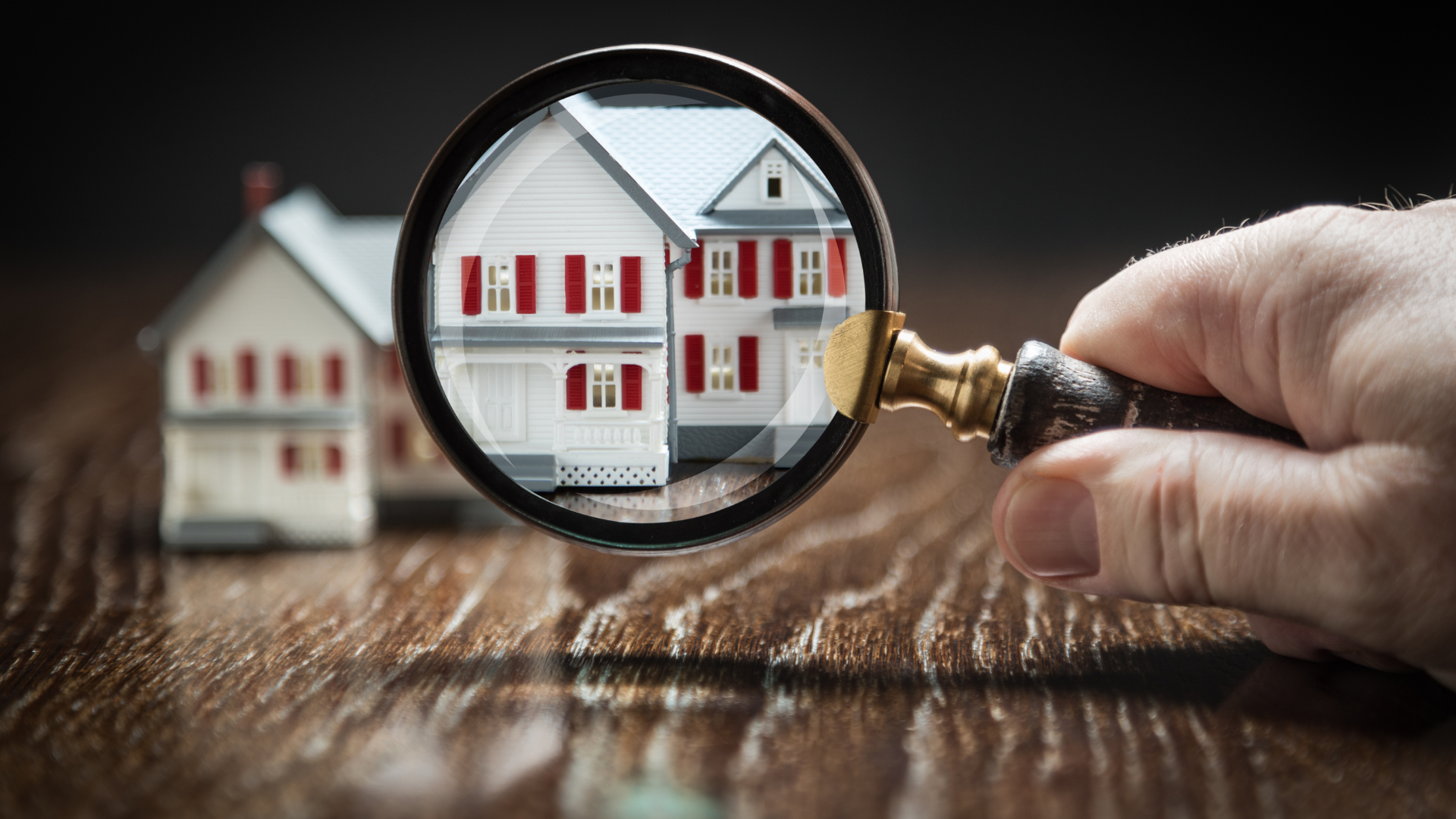 Magnifying glass over miniature house, inspecting details.