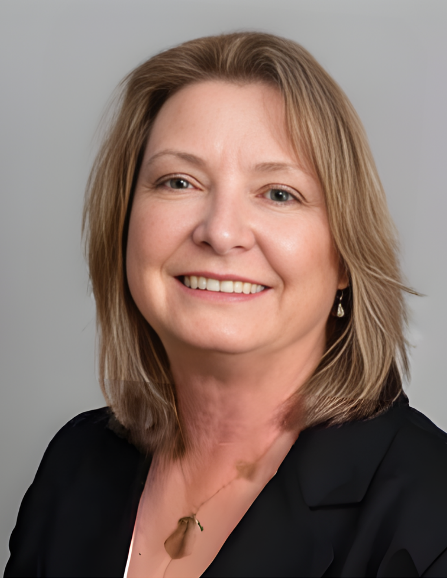 Woman with blonde hair, smiling, wearing a black blazer and necklace, against a gray background.