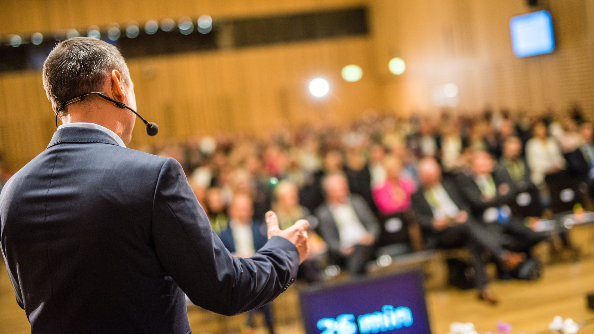 Man in suit speaking at a conference, facing a large audience.
