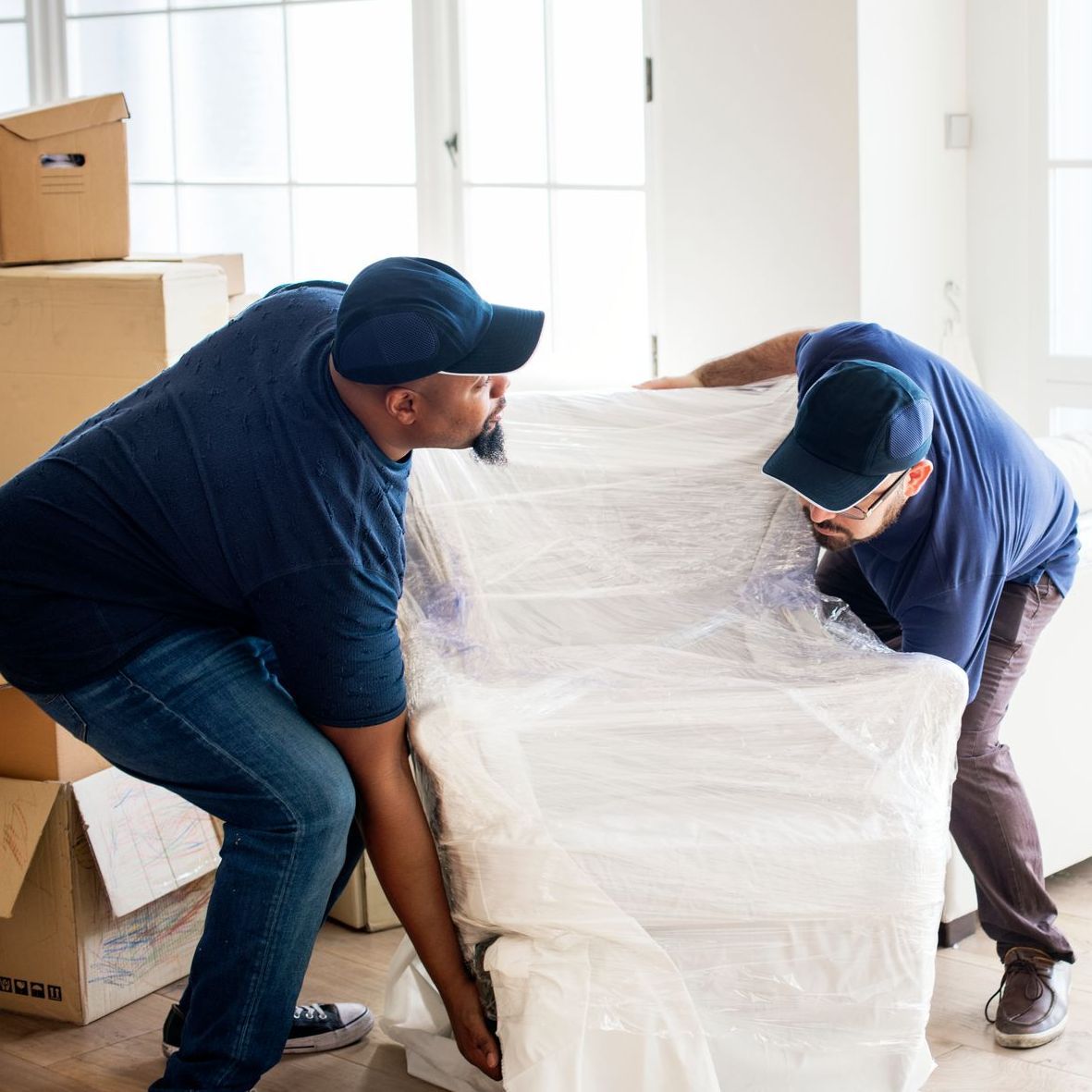 two men are wrapping a couch in plastic in a living room .