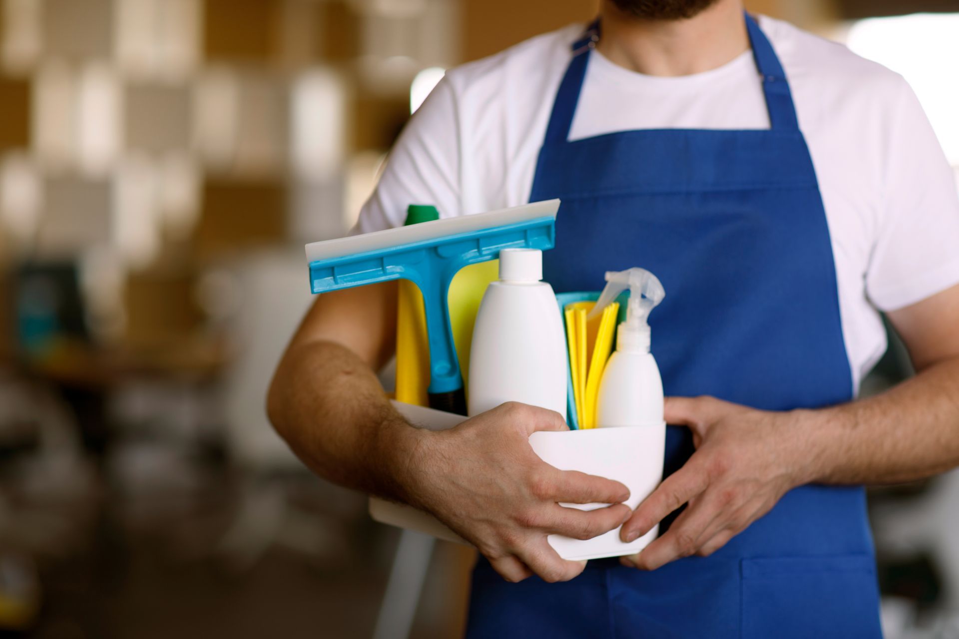 a man in an apron is holding a basket of cleaning supplies .
